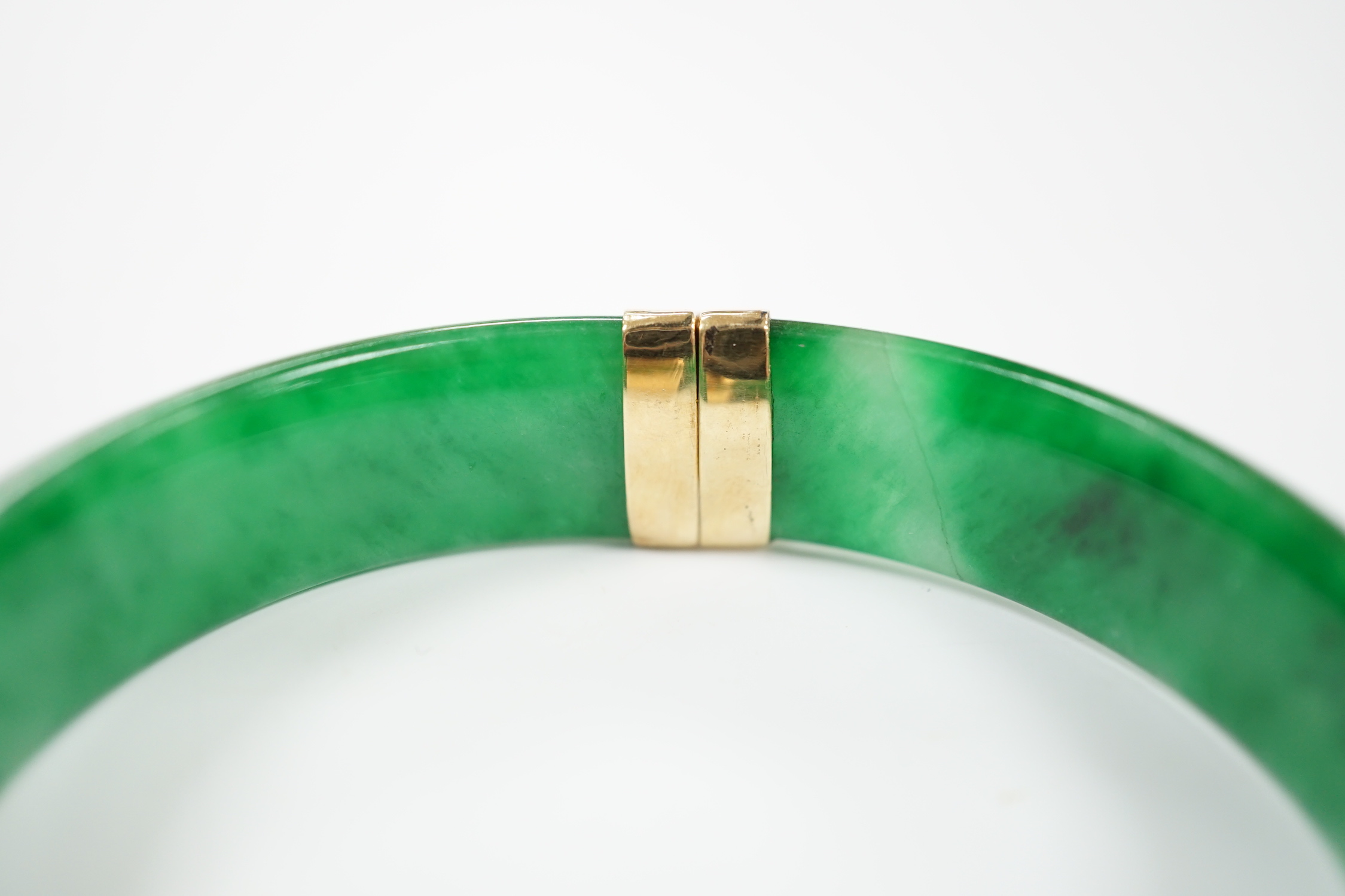 A yellow metal mounted jadeite hinged bangle, interior diameter 58mm, gross weight 59 grams.